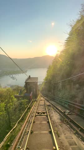 Funicular ascending through tunnel to Brunate overlooking Lake Como at sunset, scenic railway journey with dramatic exit revealing city skyline, mountains and glowing Italian landscape