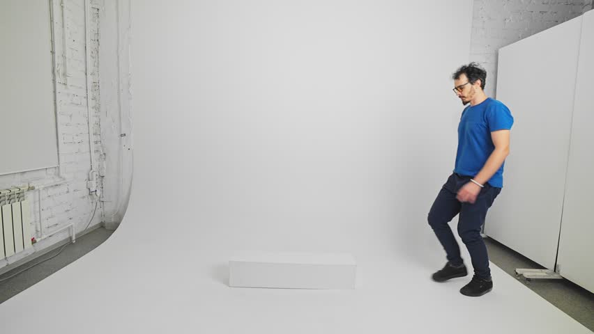 Active Caucasian man is jumping on a curb and walking carefully holding arms by side filmed in a studio in slow motion. Young adult bearded guy dressed in T-shirt and trousers is going on narrow path.