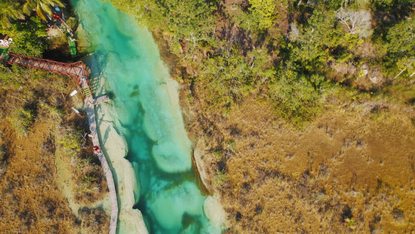 Wooden pier and Bacalar Lagoon with houses by tropical palm trees in Mexico