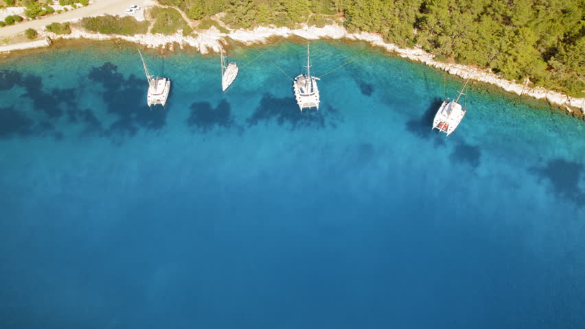 Sailboats anchored near a forested coastline with clear blue sea water in summer Greece