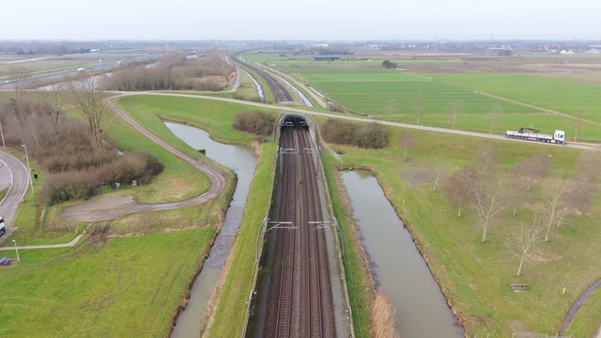 Train Enters Tunnel. Twin Railway Lines Approach Shadowy Underground Passage Amid Fields. Approaching Subterranean Tunnel With Twin Rails Through Expansive Flat Agricultural Landscape