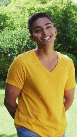 Vertical video: Man smiling, leaning in yard, camera zooming HUD moving box, dots over chest for ad. Outdoor, portrait, cheerful, yellow, tshirt, jeans, vertical video