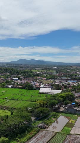 Serene rural landscape with red-roof houses, green fields, and dramatic clouds over distant hills.