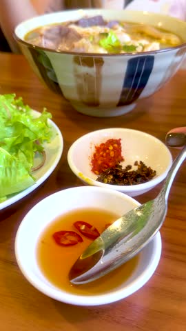 Close-up shot of person eating spicy Vietnamese beef noodle soup with fish sauce and herbs