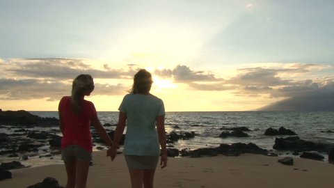 Two model released women walking together, holding hands on beach at ocean sunset.: film stockowy