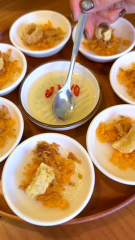 A person uses a spoon to drizzle fish sauce over traditional Vietnamese steamed rice cakes