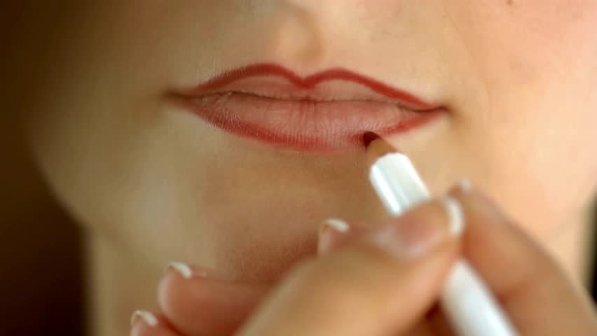 A beautiful female lips which are smeared with red lipstick. unrecognizable woman applying red lip liner before putting on lipstick, close up footage.