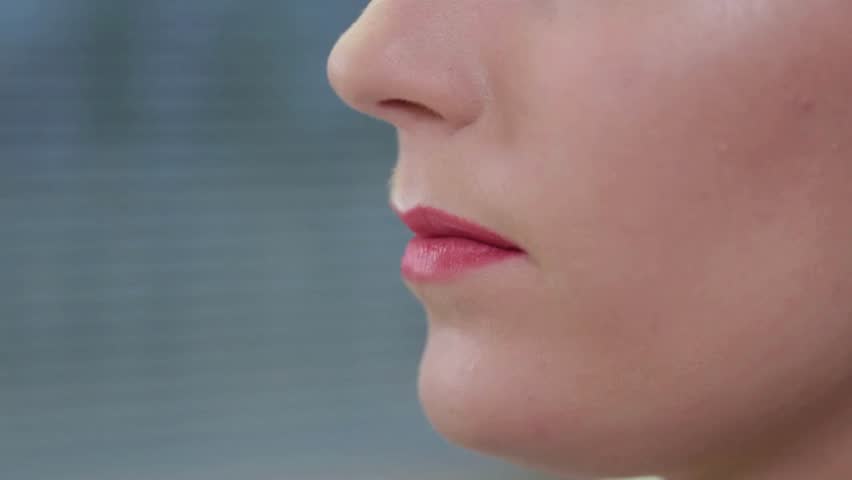 Makeup artist applies bright red lip cream on the model lips. Woman red lips, closeup view. Makeup artist paints a beautiful woman lips with lipstick.