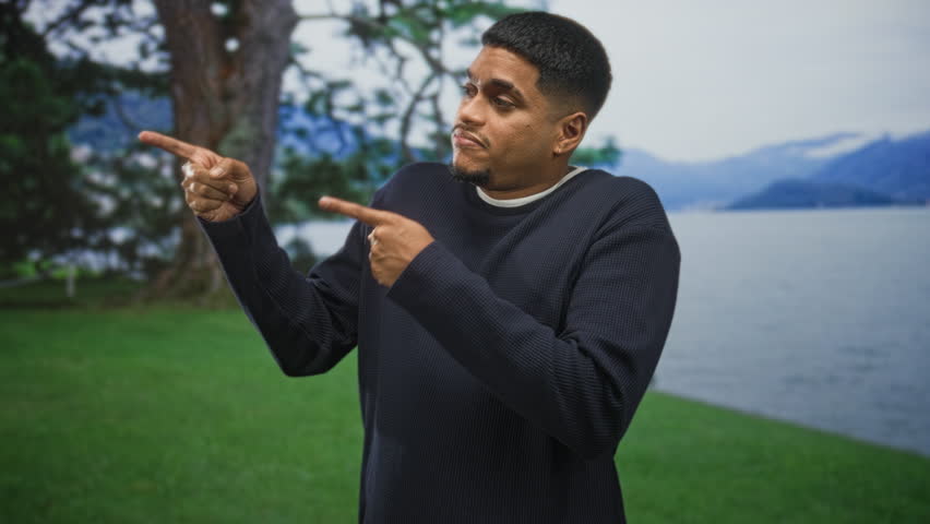 Hispanic man with beard wearing navy sweater points index fingers left and right in a forest; uncertainty indecision.