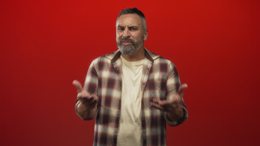 Man showing hands raised, pointing finger and open palms in red studio; frustration warning admonition stern.