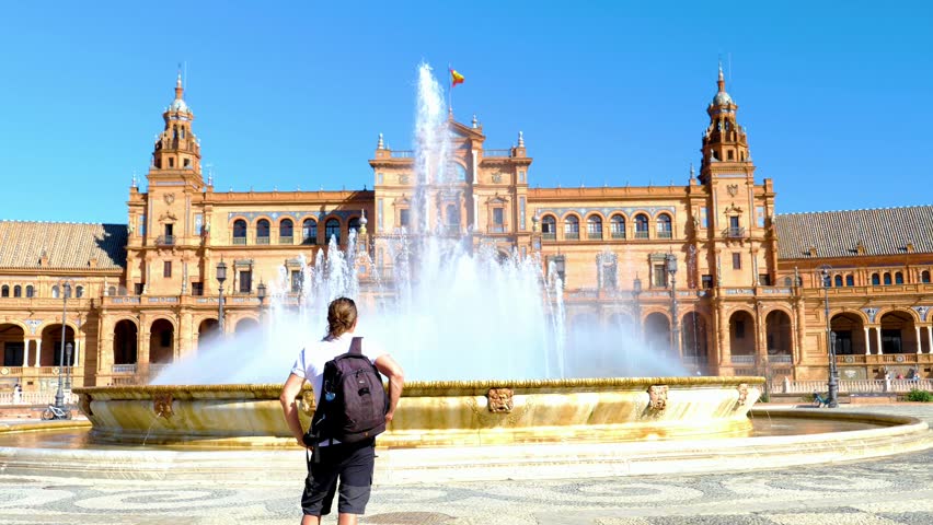 Traveler with backpack looking at the monumental fountain on Plaza de España, Seville, Spain. Renaissance Revival architecture landmark in Andalusia at sunny day. Travel and exploration concept.	