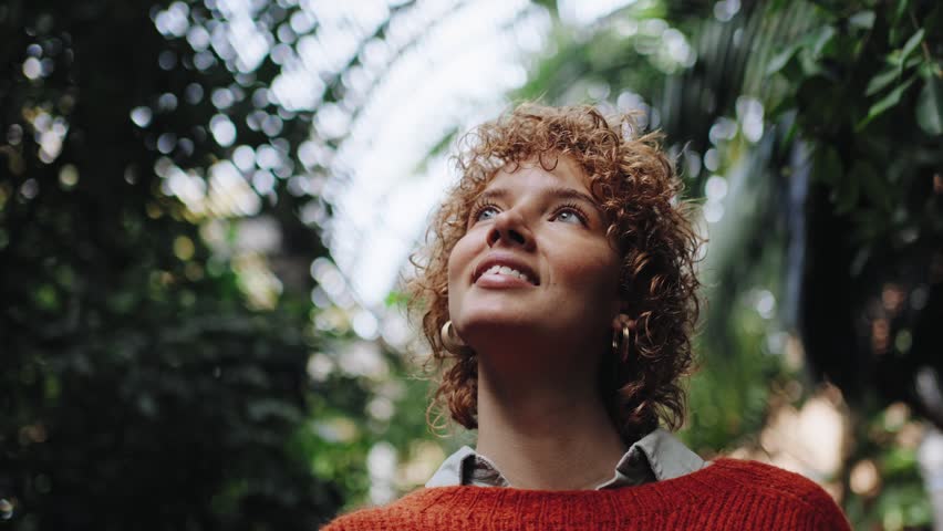 Young redheaded woman looking up surrounded by green plants and light