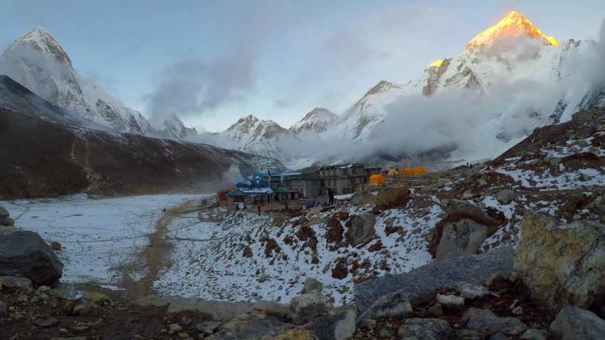 Mountain landscapes showcase stunning peaks bathed in golden sunlight while a remote base camp nestled among rocks adds human presence in this picturesque setting.