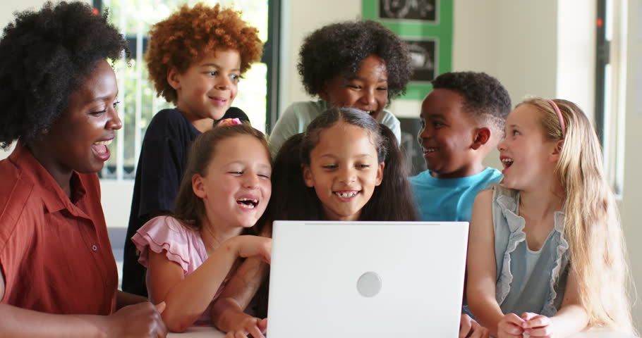 Female teacher with six kids reacting to white laptop surprise, laughing and pointing in classroom. Education, students, group, learning, collaboration, bright, posters