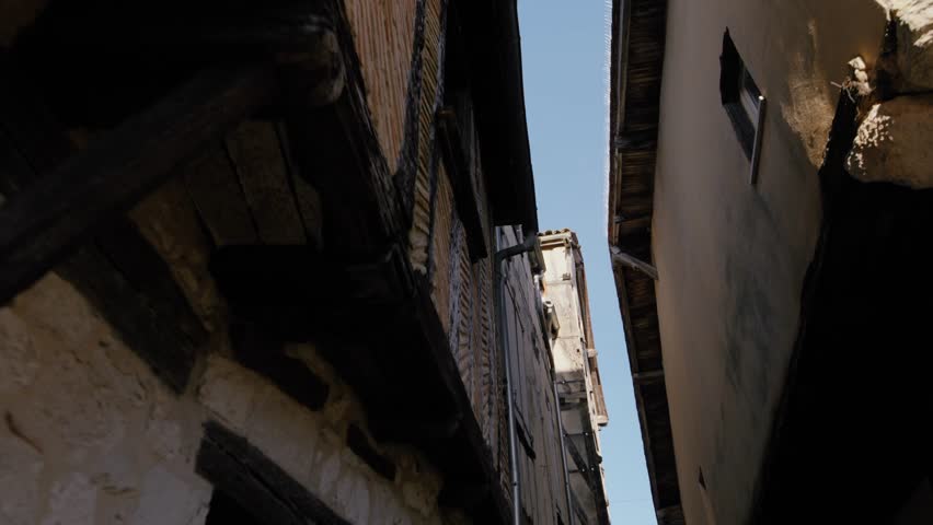 Upward view of a tight street in the bastide of Issigeac, showcasing traditional architecture and ancient stone walls. Low-angle shot.