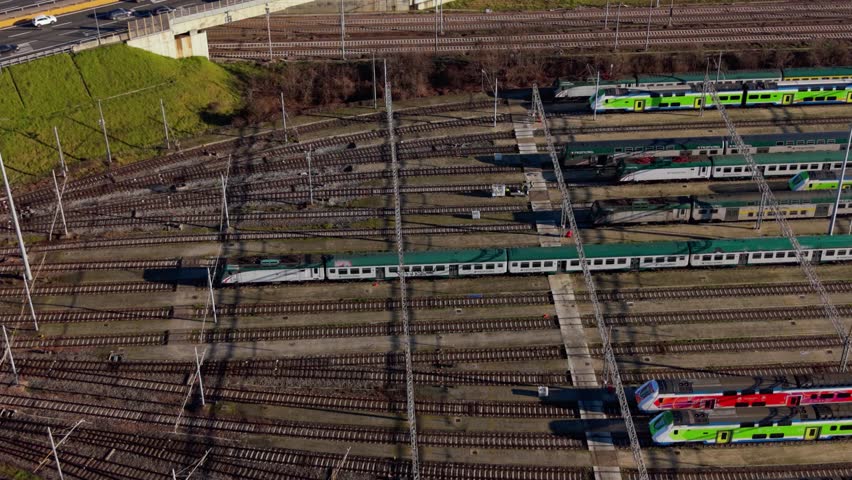 High-angle perspective of passenger trains moving slowly and maneuvering within a large, complex railway depot featuring multiple tracks and junctions