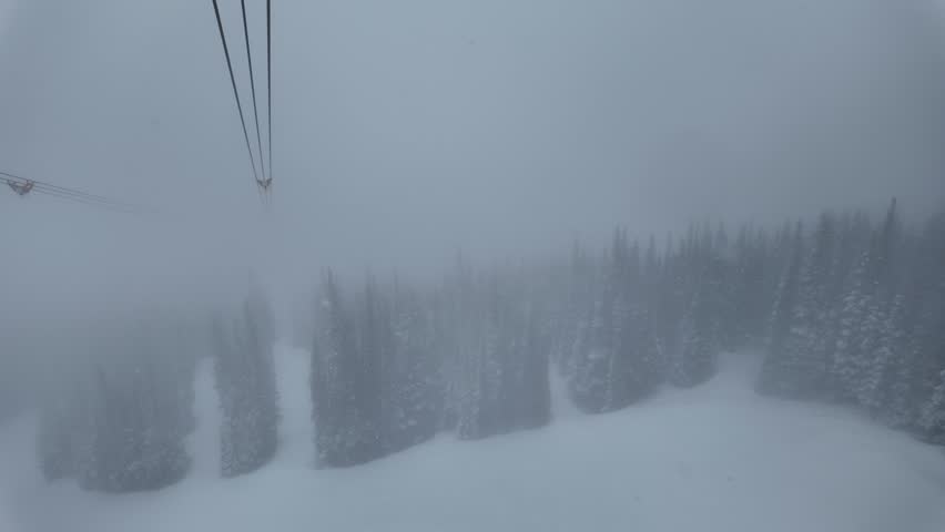 Heavy snowfall and dense fog over the pristine backcountry of Whistler. Aerial POV riding the PEAK 2 PEAK gondola connecting Whistler Blackcomb Mountain to Whistler Mountain Ski Resort.