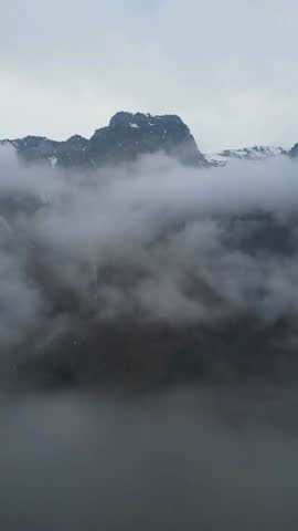 Dramatic landscape of a rugged mountain peak partially shrouded in thick fog low-hanging clouds