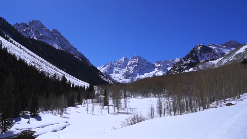 Bright winter panorama of the Maroon Bells Pyramid Peak 14ers rising above a snow-covered valley and bare aspens, capturing a crisp mountain sunny morning blue sky Aspen, Colorado Rocky Mountains