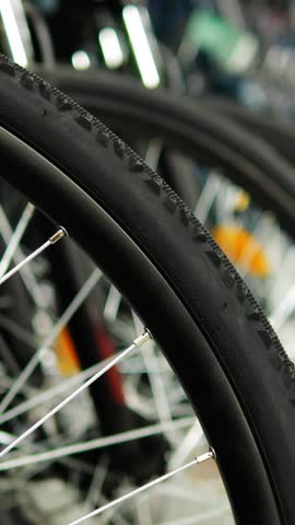 Front tire of city bike stands in row of cycles at local sports store. Thin metal spokes with smooth rubber surface highlight quality for daily rides