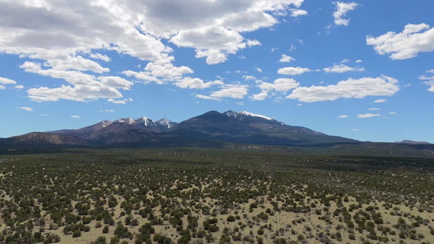 This drone flight travels over a forest land toward the snowy summit of Humphreys Peak. The vast nature landscape showcases the high altitude beauty of the San Francisco Peaks.