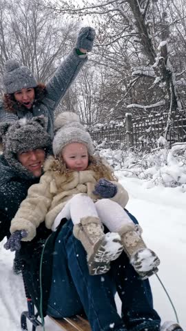 Family sledding in winter. outdoor winter activity. Happy, laughing, playful family of 4 is enjoying of sledging their children on snowy road, in forest, during snowfall. family is having fun