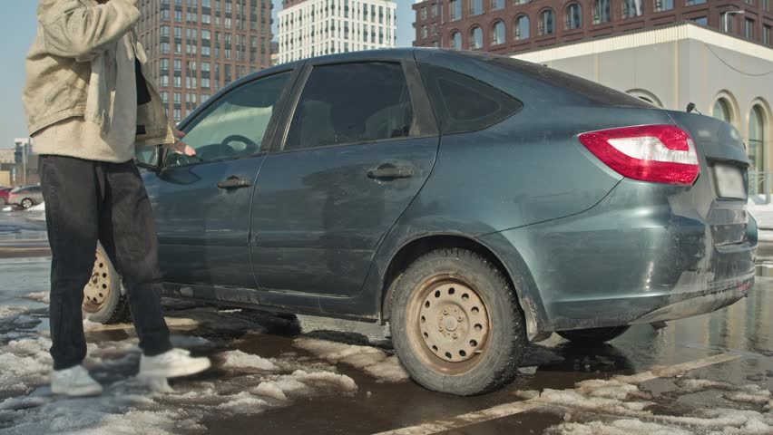 Driver gets out of broken car in winter and angrily argues while talking on the phone in snowy parking lot.