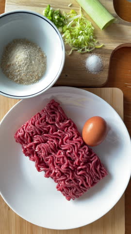 Hands Cracking Fresh Egg into Raw Ground Beef Mince for Meatball Preparation with Breadcrumbs and Leeks on Wooden Table