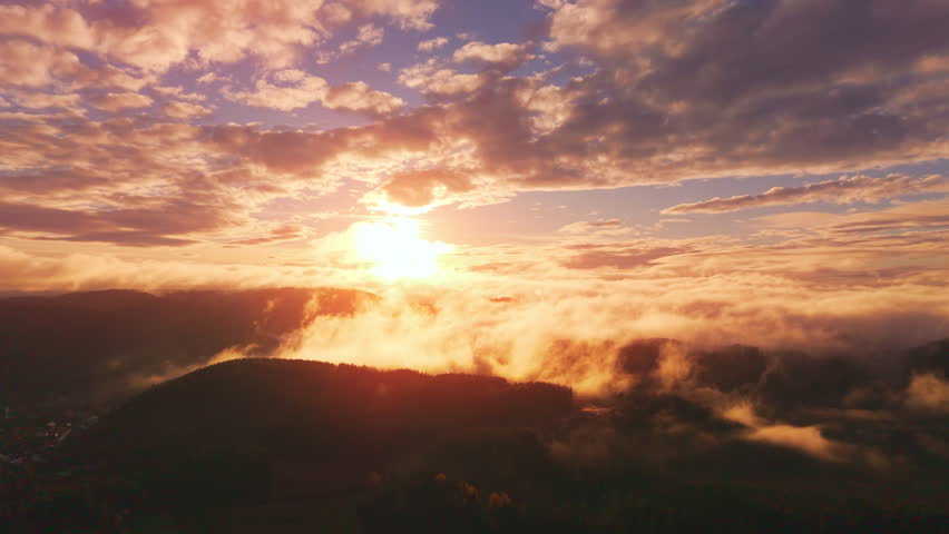 Aerial view of a golden sunset over fog with rolling hills and glowing clouds. Cinematic landscape in northern Europe.