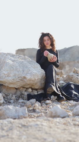 Woman in black dress sitting on rocks in desolate landscape