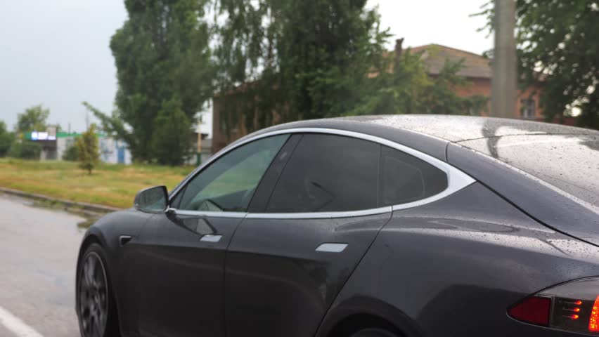 Ecology friendly car driving at urban road on sunny rainy day. Modern electrical automobile riding moving along motorway. Electric vehicle riding through empty highway. Concept of green innovation