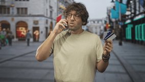 Man on street holding phone to ear and fanning creditcard with hand, looking concerned while assessing cards; concern payment decision. - Powered by Shutterstock - Get 15% off with code: PIKWIZARD15