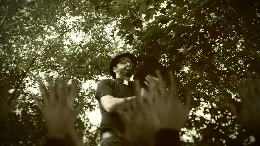 Religious man, reverend or priest wearing a clerical collar and thumping a bible to his congregation. Preacher preaching the gospel to a group of followers in a rural setting.