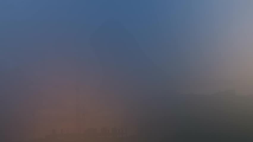 Rain falls from passing clouds over the city and construction cranes at sunset.