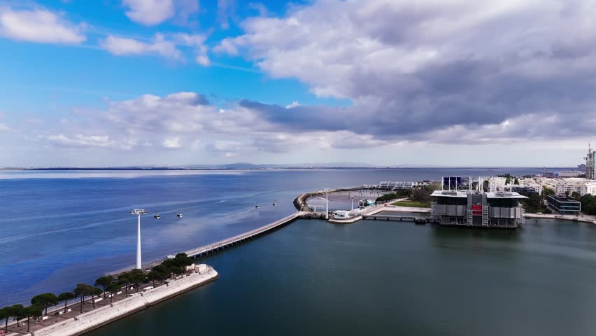 Aerial view of cable cars over Tagus river and waterfront under dramatic clouds. Lisbon, Portugal