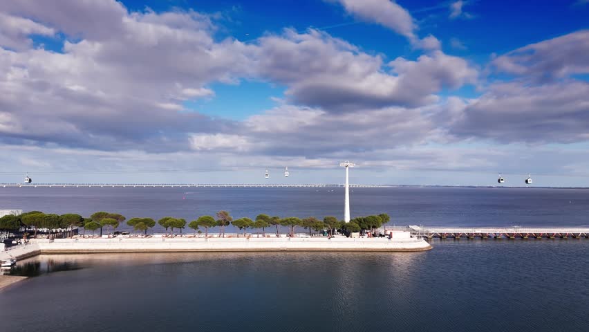 Aerial view of cable cars over Tagus river and waterfront under dramatic clouds. Lisbon, Portugal