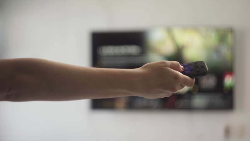 Close-up of a female hand holding a remote and channel surfing on a smart tv. Someone browsing through an on-demand video library