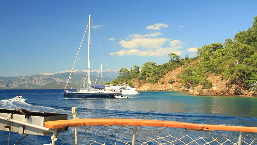 View from boat deck of a large sailboat anchored in Gocek cove with speedboat wake and mountain backdrop, Mugla, Turkey