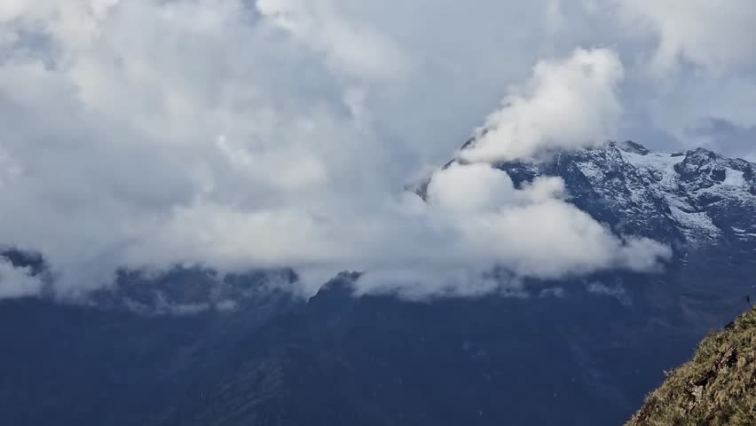 Inca Trail, Peru - 25 June 2024. Clouds wrap around a snowy mountain summit, with rugged slopes and shadowed ridges below under overcast conditions.