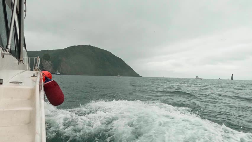 A motorboat fast sails across the sea during cloudy, choppy weather, as seen from the side. Waves splash in all directions