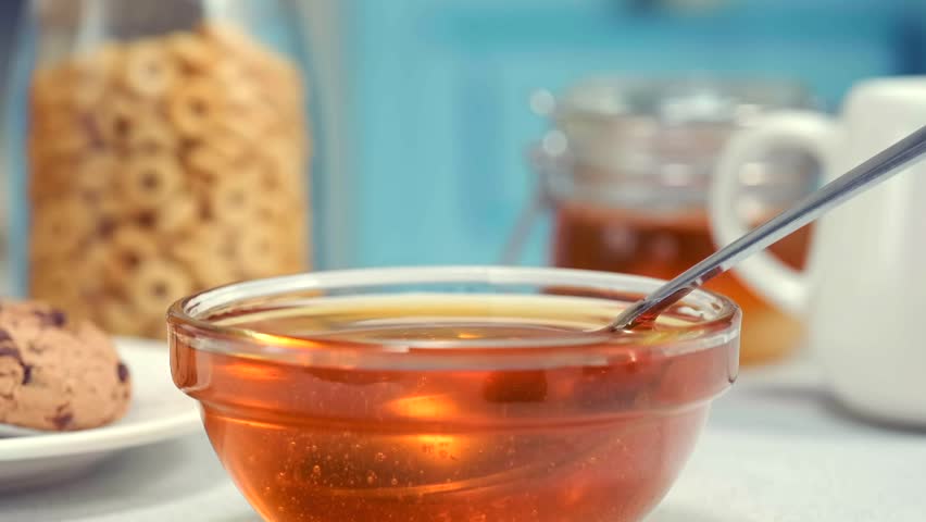 Honey dripping from spoon into glass bowl macro food texture dessert syrup copy space