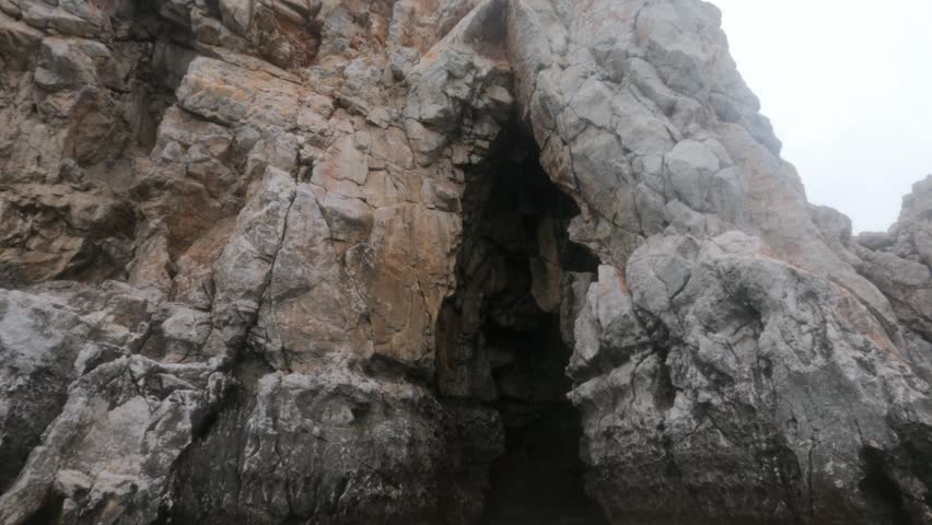 Rugged limestone cave opening carved into coastal cliffs at Souda Bay, Chania, Greece. Misty overcast sky frames jagged rock formations at a premier freediving location.