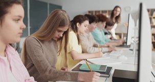 Students teenagers in classroom computers learning. Teens focus at screens as teacher supports, blending note taking and school tech practice for tasks. Clear concept of collaborative learning. - Powered by Shutterstock - Get 15% off with code: PIKWIZARD15