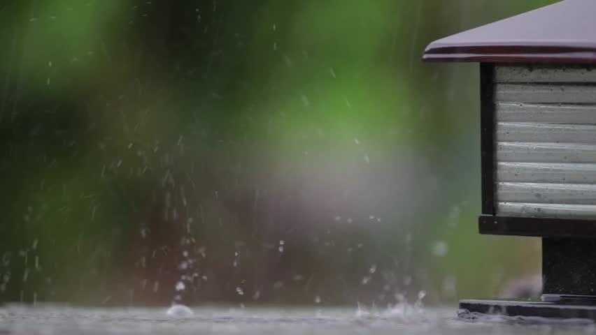 Raindrops hit a rooftop ledge creating splashes with soft green background during a heavy rain shower