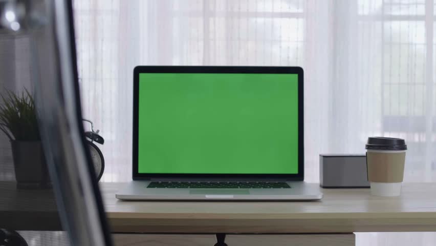 Static video of laptop with chroma key screen on clean desk by window with alarm clock plant and takeaway coffee