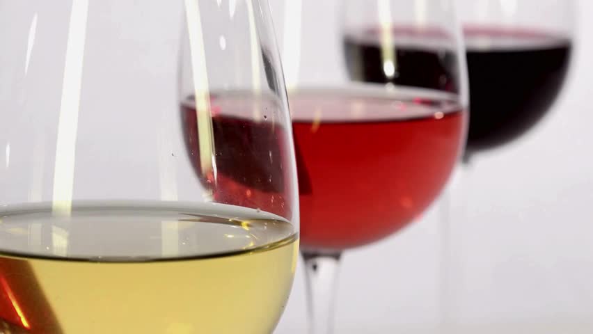 Three glasses of wine are prominently displayed, containing white, rosé, and red varieties. Friends laugh and converse in a cozy indoor setting during the evening hours.