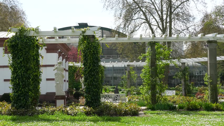 Palmengarten Frankfurt with pergola, statues and greenhouse surrounded by lush greenery and blooming plants in spring daylight