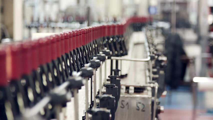 bottling line is seen in operation, with bottles being filled and capped in a winery. Workers manage equipment and ensure quality control during the bottling process.