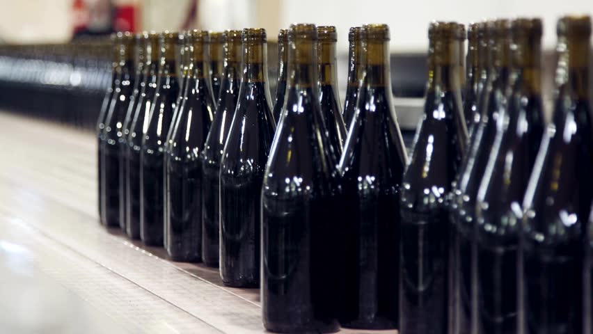 A detailed view of the bottling line at a local craft beverage facility. Workers meticulously fill and prepare dark bottles for distribution during a busy afternoon shift