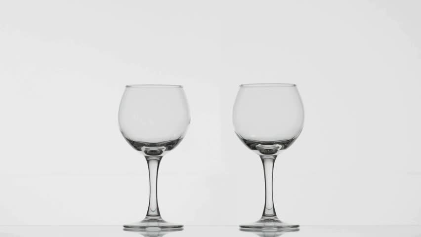 A hand pours rich red wine from a bottle into two empty glasses. The minimalist backdrop enhances the elegant presentation of the wine and glassware